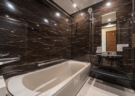 ダークマーブルの壁面が印象的な高級感あふれるバスルーム。ゆったりとした浴槽と広めのスペース設計で、贅沢なリラックスタイムを叶えます